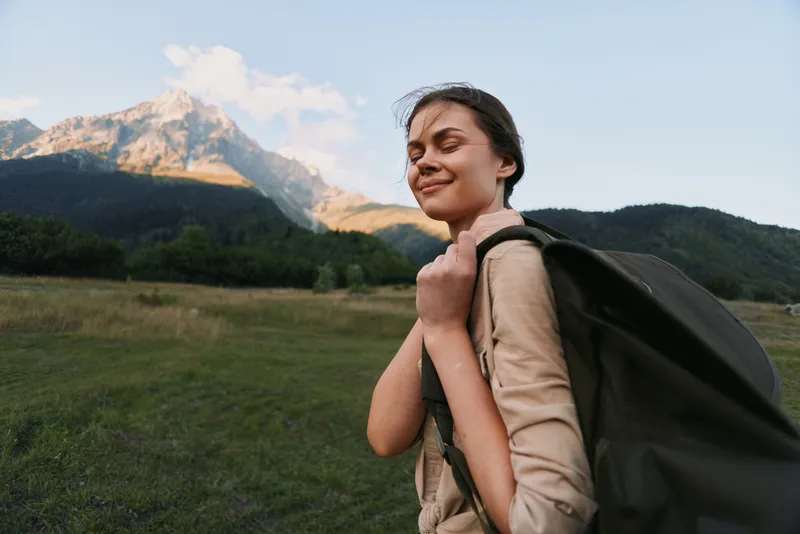 A young woman with a backpack enjoys a peaceful moment outdoors in nature with mountains in the background during a sunny day. Concept for lifestyle and adventure.