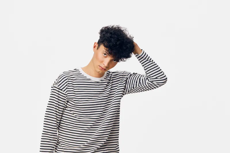 young man in striped shirt looking thoughtful and casual with hand in hair against plain white background, natural expression, modern style