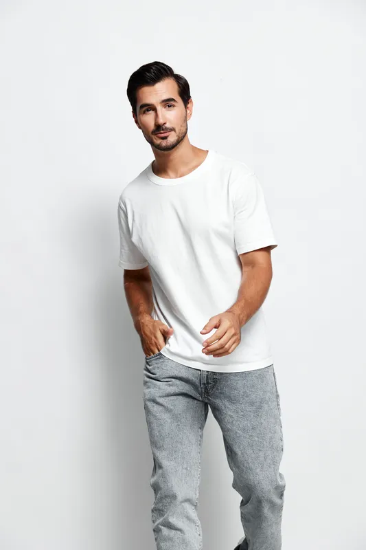 Full body smiling man dressed in casual white t-shirt and patterned jeans, looking at the camera with a friendly expression, isolated on plain solid white background.