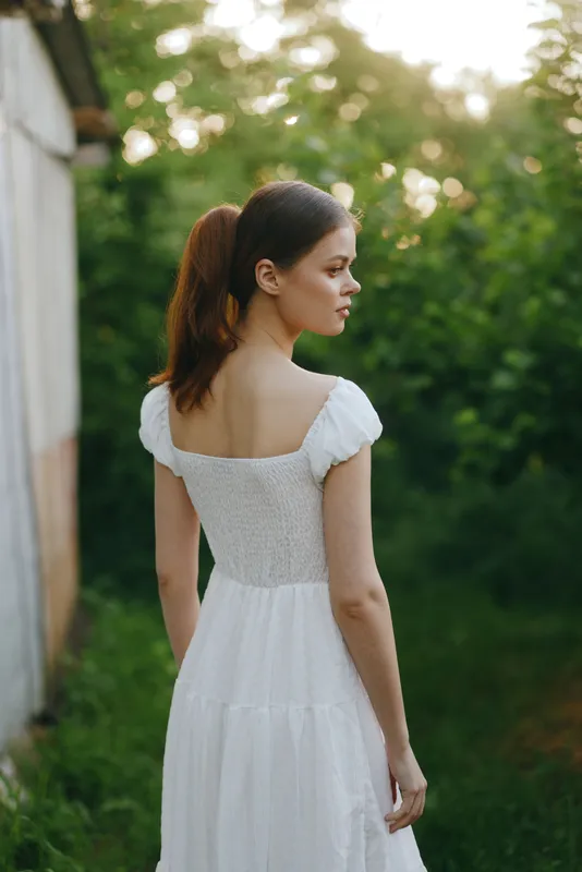 Young woman in a white summer dress standing in a green garden, capturing tranquility and nature s beauty, ideal for seasonal themes of relaxation and femininity