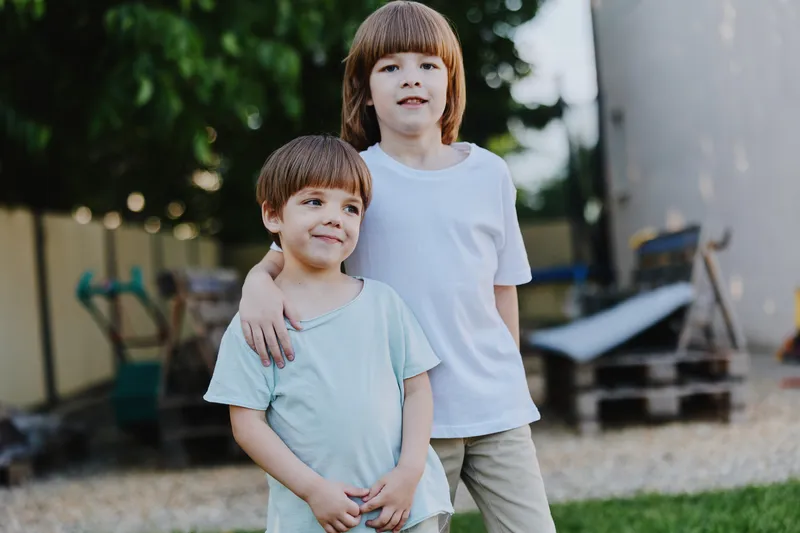 Two cheerful boys enjoying their time outdoors, wearing casual clothes, surrounded by greenery. Perfect for childhood memories and family themes.