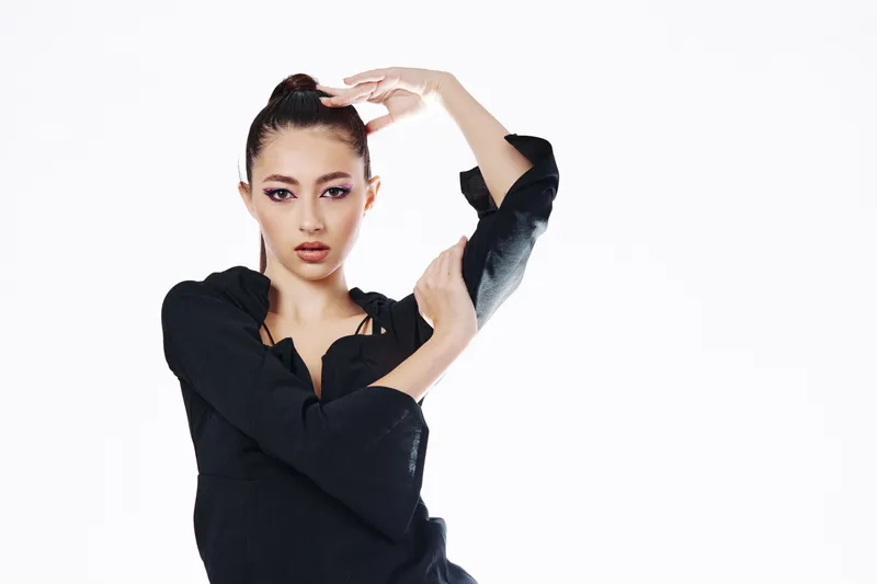 Fashion model with strong makeup and sleek hair poses in a black outfit on white background. Concept of beauty, creativity, high fashion, and elegant attitude.