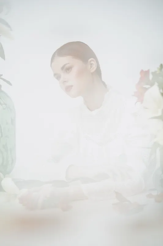 Ethereal portrait of a young woman in a white blouse, expressing tranquility amidst soft floral elements and a pastel background