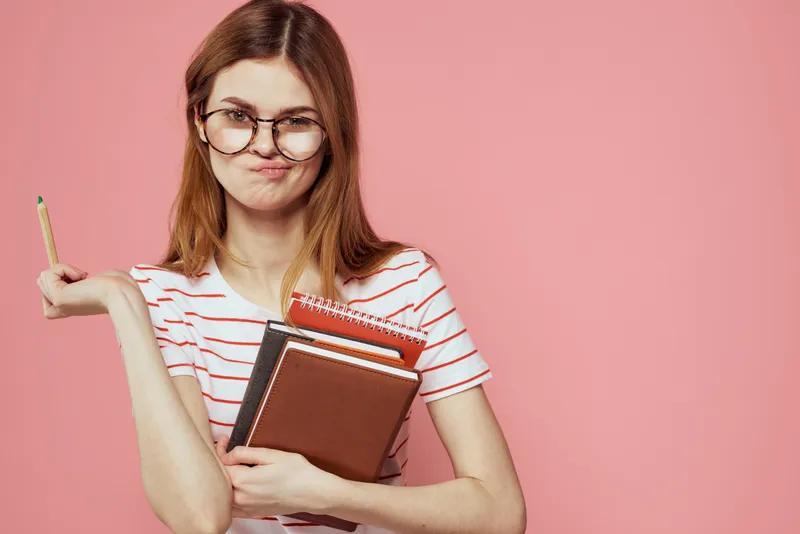 Молодая студентка с книгами на розовом фоне, в очках на лице, кадрированный вид, учебное заведение