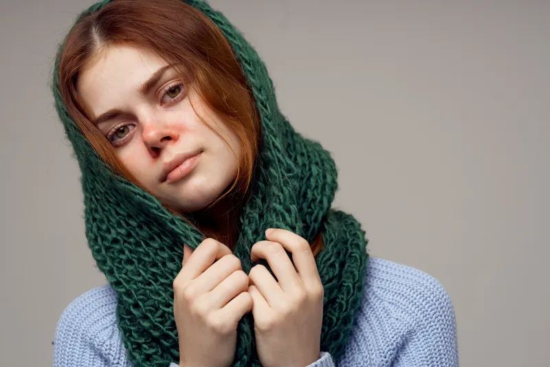 Женщина с вязаным шарфом на голове, что указывает на проблемы со здоровьем, насморк; на ней синий свитер