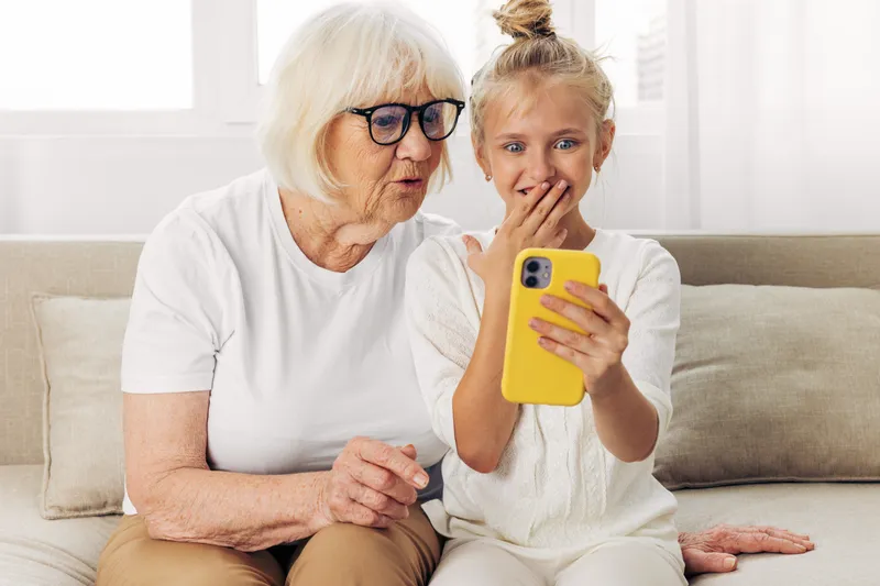 Семья обнимается на диване, улыбается, смотрит в телефон