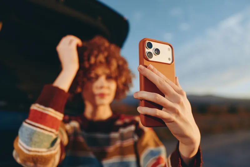Woman selfie with smartphone outdoors lifestyle, young friend in car background, street travel moment, natural daylight, calm hands holding device