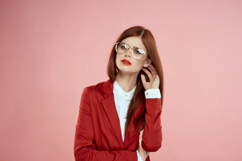 Женщина в красной куртке, в очках, с красными губами и длинными волосами, розовый фон