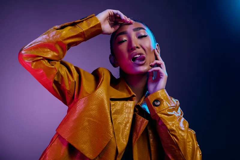 Привлекательная азиатская модель с ярким макияжем, синими губами и неоновыми волосами на разноцветном фоне