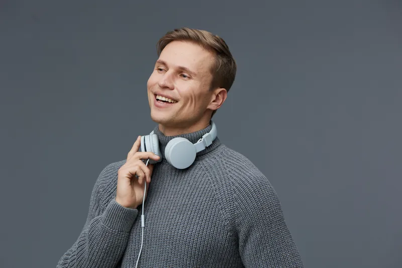 Smiling man with headphones looks away isolated on gray background. Casual clothing, joyful expression, contemporary style. Suitable for lifestyle, music, leisure, technology, modern, advertisement co