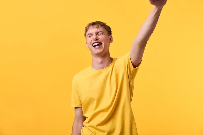 Joyful man in a yellow shirt raises his arm in celebration against a bright yellow background, conveying energy, success, and a positive mood for marketing and lifestyle campaigns