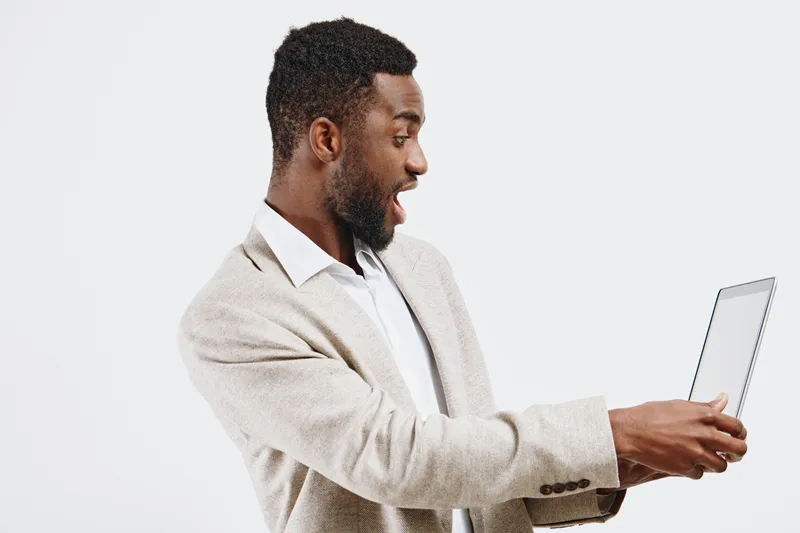 Smiling man in beige blazer using tablet device isolated on plain white background. Happy male with beard, casual professional outfit, engaging with technology, studio portrait, positive mood, modern 