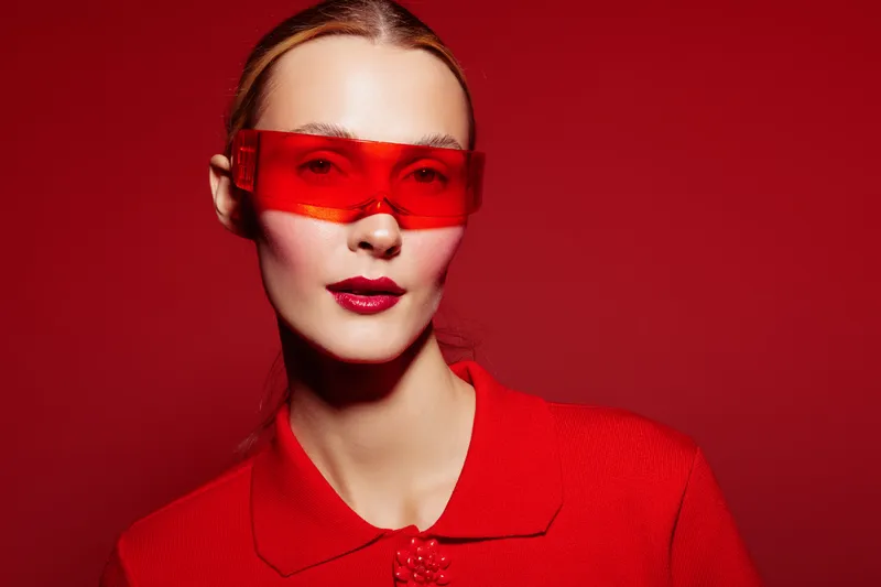 Portrait of a stylish woman wearing red sunglasses and a red outfit against a red background. Fashion concept with bold colors and modern accessories in studio lighting.