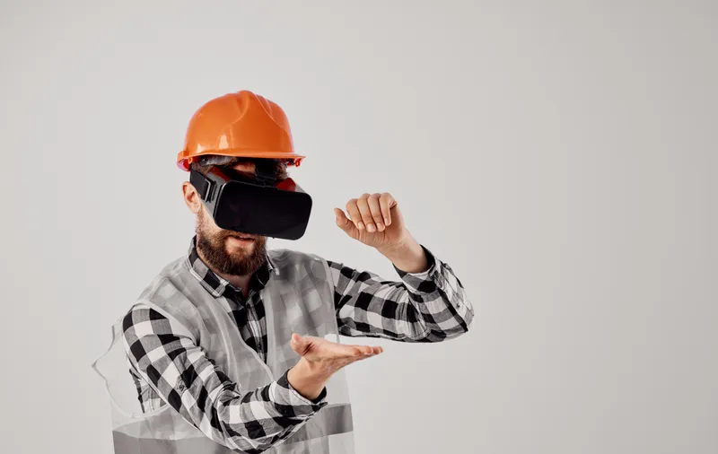 Архитектор в 3D-очках виртуальной реальности жестикулирует руками, на голове у него оранжевая каска