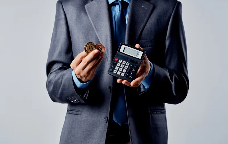 Бизнесмен с калькулятором в руках и криптовалютой Bitcoin, обменный курс богатства