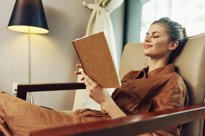 Безмятежная молодая женщина погружена в чтение книги, отдыхая в стильной гостиной
