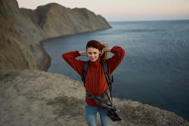 Женщина на фоне осеннего пейзажа: горы, море, пляж, рюкзак