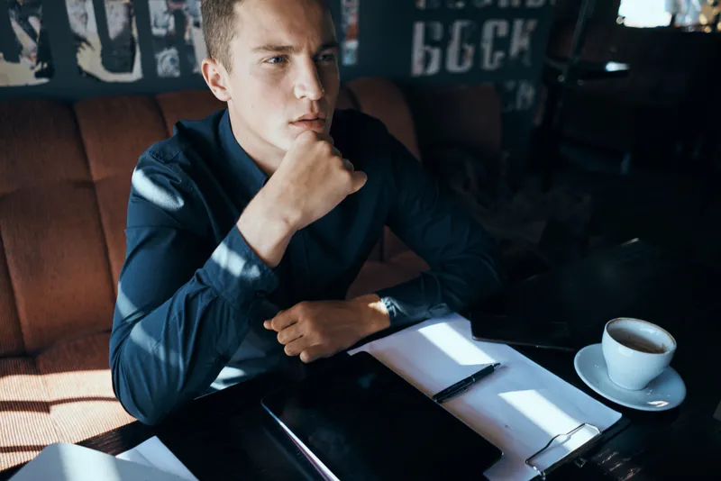 Бизнесмен-фрилансер с ноутбуком в кафе за столом, с документами менеджера и чашкой кофе, позирующий как модель