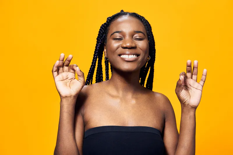 Happy African woman smiling with a meditative gesture against a bright yellow backdrop, radiating positivity and joy