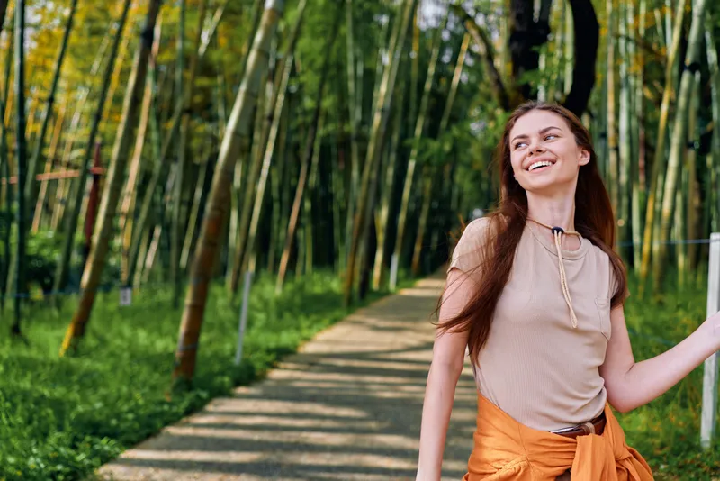 woman smile walking bamboo path forest nature casual young woman walking along a sunlit bamboo path, smiling relaxed and carefree, portrait outdoors with summer greenery and peaceful trail atmosphere
