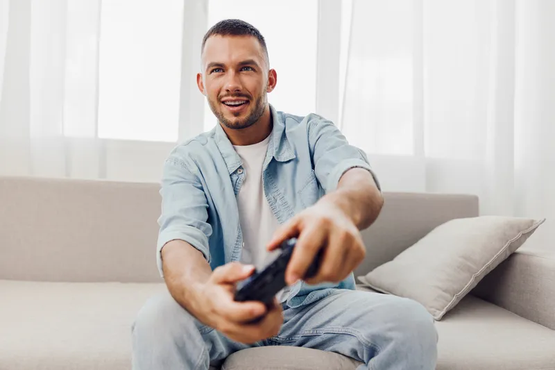 Engaging man enjoying a digital detox, relaxed on a couch, smiling and unwinding from technology's grasp while embracing authentic imperfection.