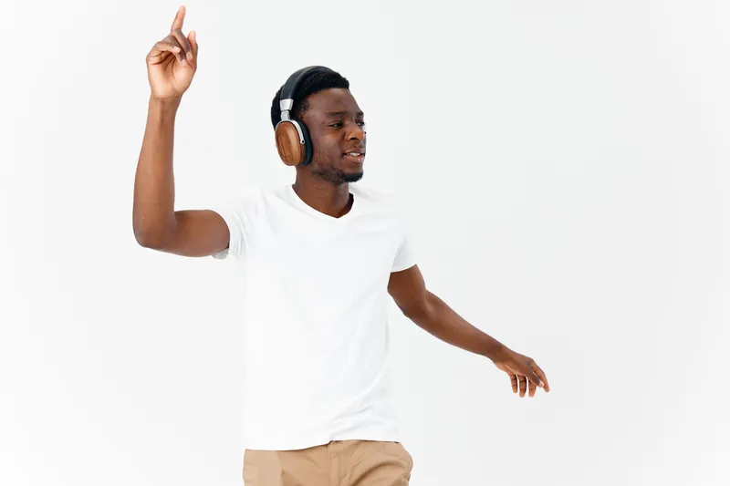Веселый мужчина в белой футболке с наушниками слушает музыку на светлом фоне