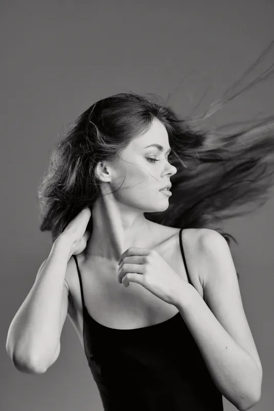 Black and white portrait of a young woman with flowing hair wearing a sleeveless top in calm expression
