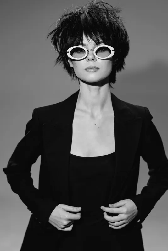 Black and white stylish woman wearing sunglasses and a blazer posing confidently with messy hair.