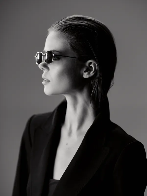 Black and white portrait of a stylish woman wearing sunglasses and a blazer with a confident expression.