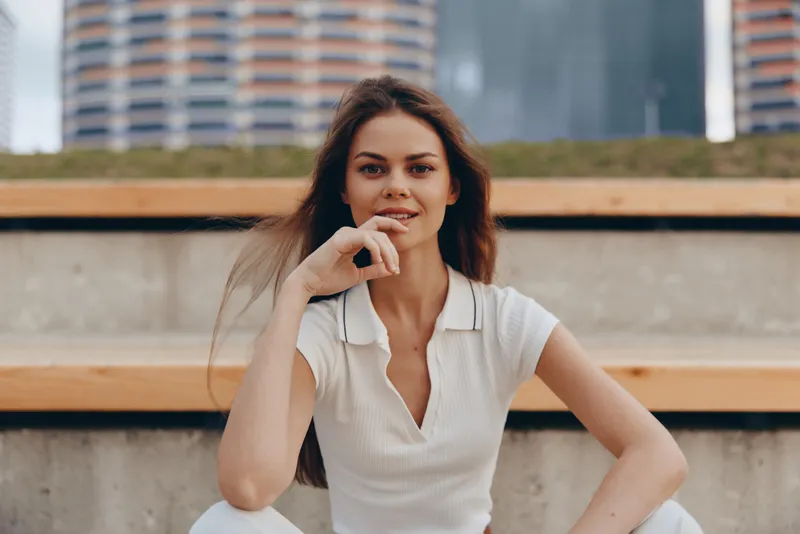 Confident woman in business attire sitting outdoors, radiating positivity and professionalism against a modern urban background with a natural color palette.