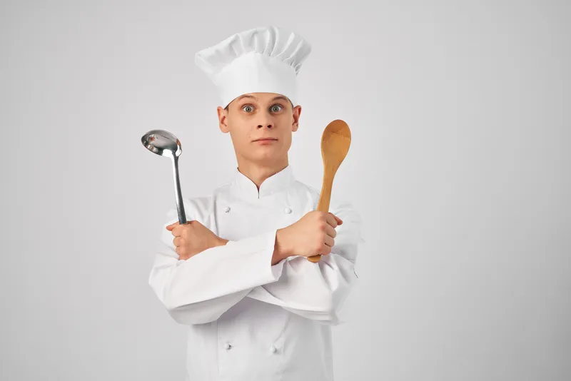 Мужчина в форме шеф-повара работает на кухне ресторана, используя кухонные принадлежности