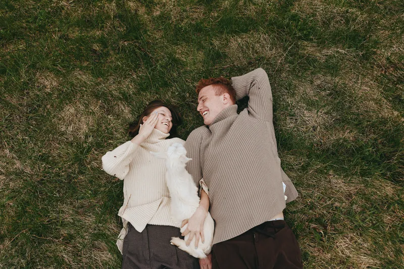 Couple romance outdoors grass sweaters together smiling affection relaxation lifestyle moment on grass, conveying warmth and playful connection in natural light