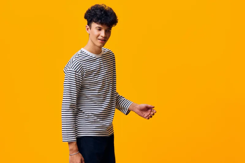 young man wearing striped shirt poses confidently against bright yellow background, showcasing casual style and relaxed mood in vibrant setting