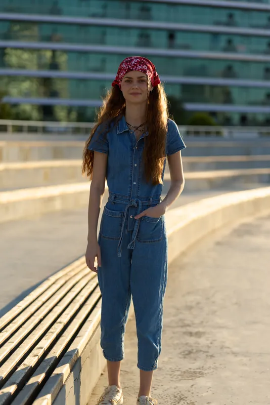 Lifestyle woman in modern boho-western denim street style wearing a red bandana, standing outdoors with warm film color tones and casual summer vibe.