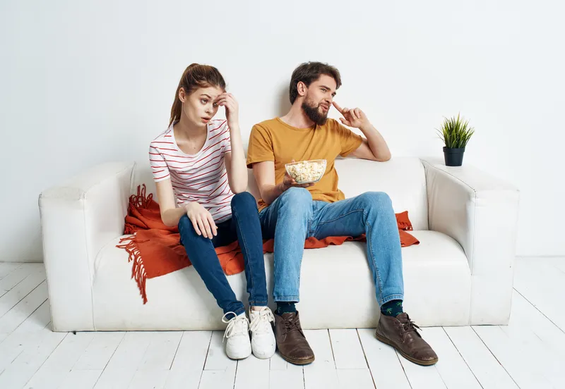Веселые мужчина и женщина на диване с попкорном и красным пледом, цветок в горшке, эмоции