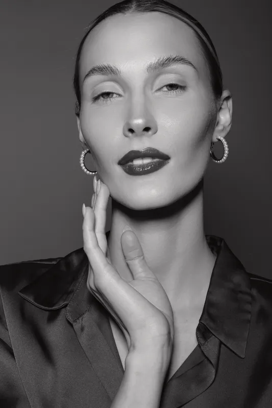 Close-up of a fair skinned Caucasian woman with sleek hair and glossy lips posing with hand near face. Studio portrait with elegant mood and fashion concept.