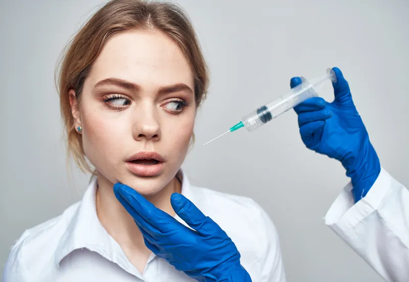 Женщина, шприц для анестезии и инъекции ботокса, врач в синих перчатках
