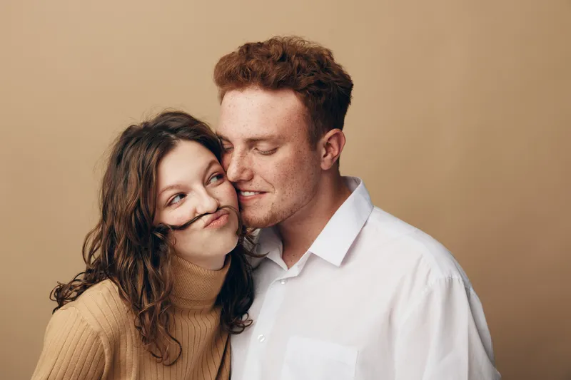 Young couple in casual clothes share a tender moment, smiling and close together against a beige background. Concept of love, affection, intimacy, and relationship happiness.