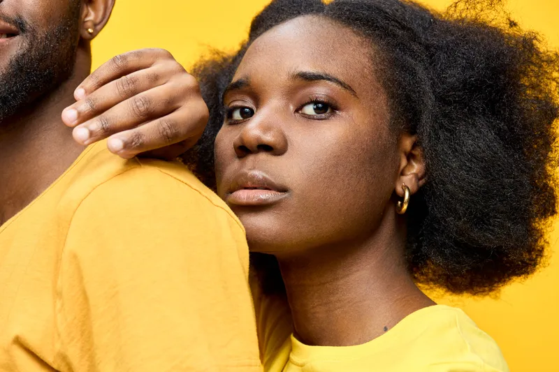 Young African American woman expressing joy and confidence, wearing a yellow shirt against a bright yellow background, showcasing vibrant emotions of happiness and togetherness