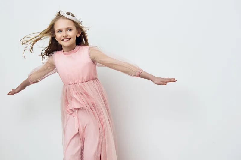 Happy girl in a pink dress twirling joyfully against a soft white background, embodying innocence and playfulness Ideal for children s fashion and joyful moments