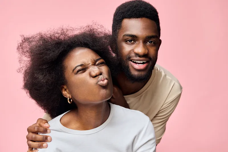 Happy African couple smiling and having fun together, showcasing joy and connection against a soft pink background, with vibrant emotions reflected in their expressions