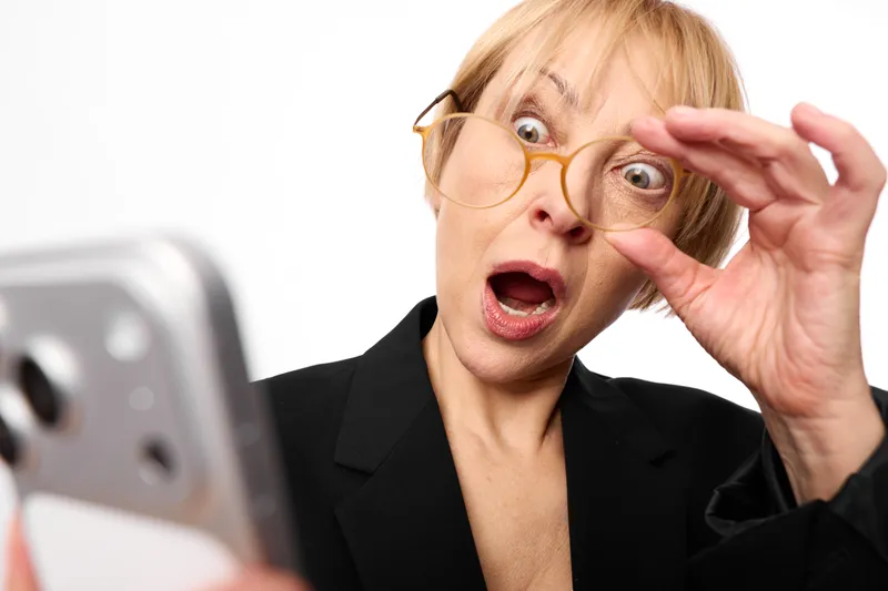 Surprised business woman adjusts glasses with her hand for a smartphone selfie, office portrait, eyewear closeup, white background, modern technology feeling