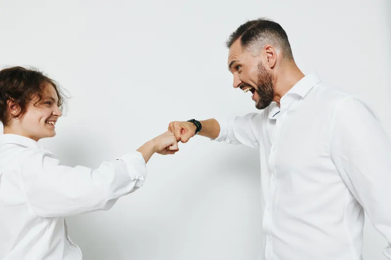 Professional man and colleague share a fist bump, signaling teamwork and positive energy. Isolated colored background boosts corporate vibe, confidence, and friendly drive in a business setting.