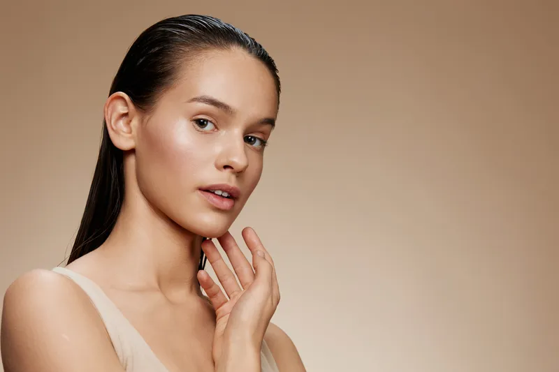 Close up portrait of a young model with smooth skin and wet hair, expressing serenity and confidence against a neutral background, emphasizing beauty and skincare concepts