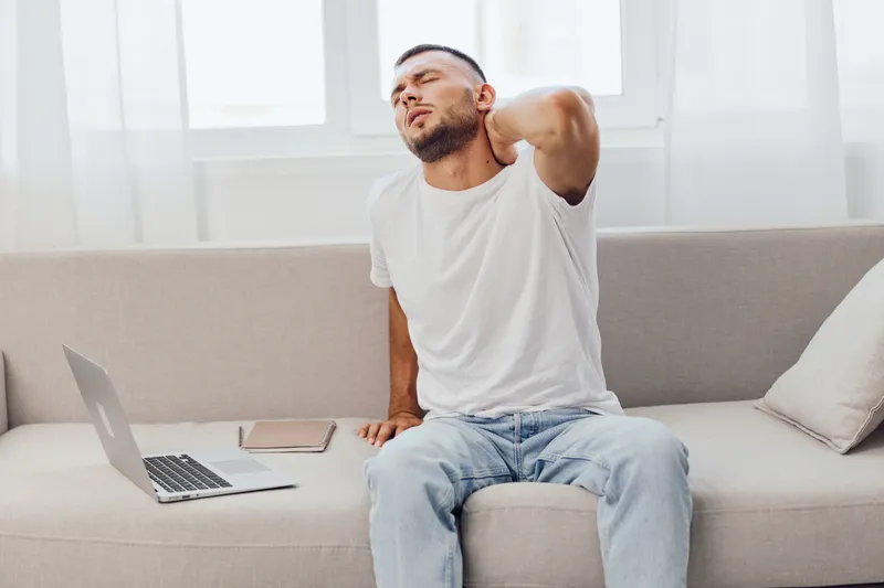 A man experiencing stress and discomfort while working from home, showcasing the blurred lines between work and personal life, reflecting modern challenges.