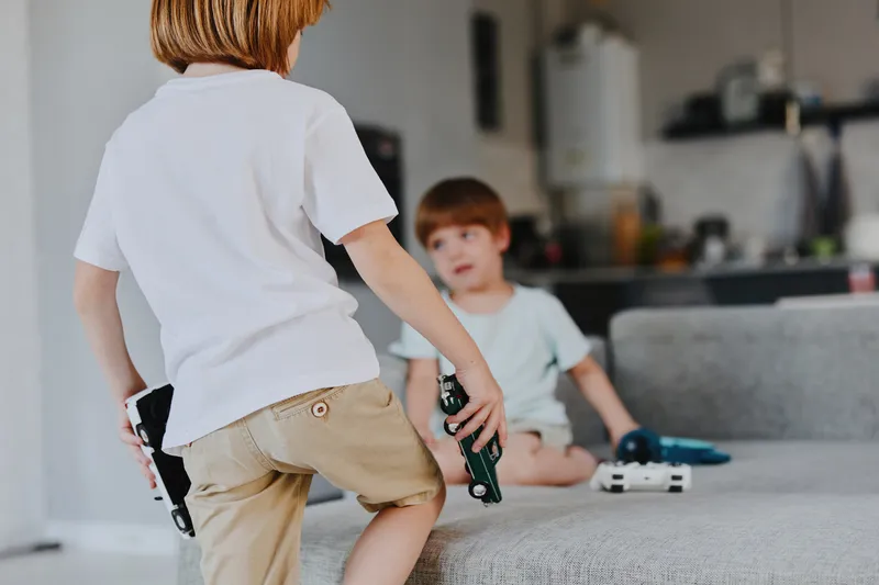 Two boys playing in a cozy living room, showcasing their favorite toy cars while enjoying a fun and playful moment together. Bright atmosphere enhances their joy.