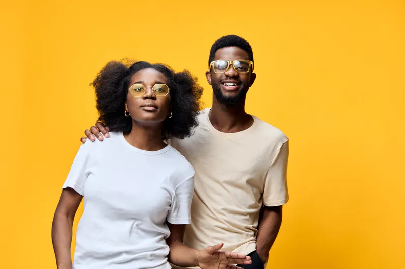 Young African models wearing trendy sunglasses, posing joyfully against a vibrant yellow background, expressing happiness and confidence in casual summer attire