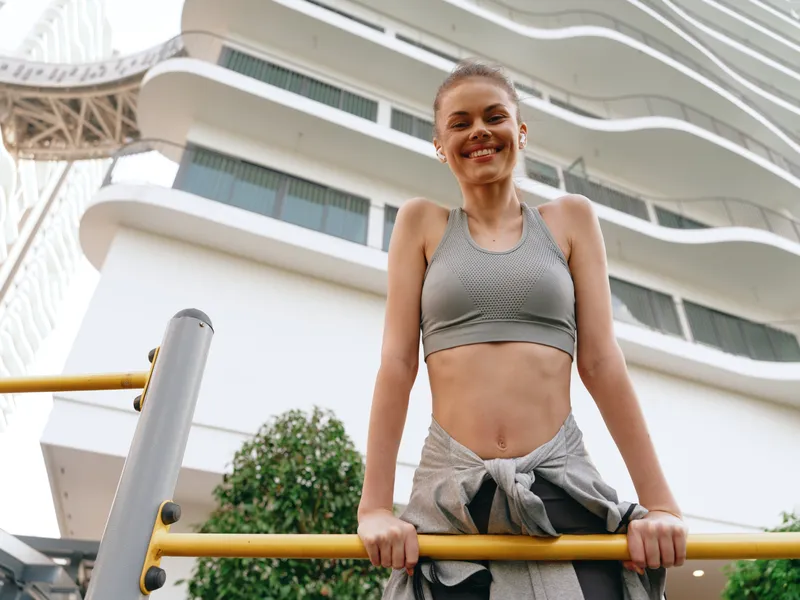 Спортивная девушка улыбается, выполняя подтягивание в солнечный день