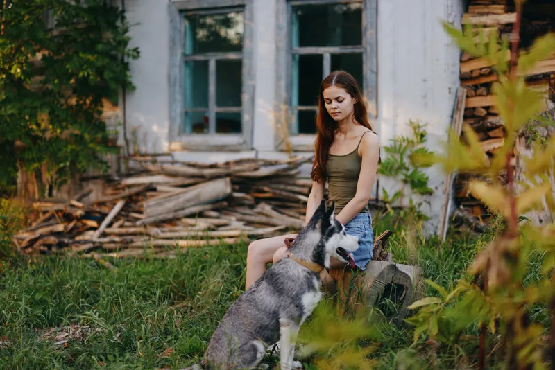 Женщина и её хаски весело играют на улице в парке среди деревьев, улыбаются, показывая зубы, во время осенней прогулки со своим питомцем