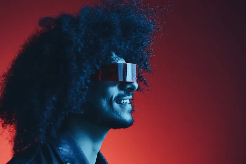 Портрет стильного мужчины с кудрявыми волосами на красном фоне в модных очках